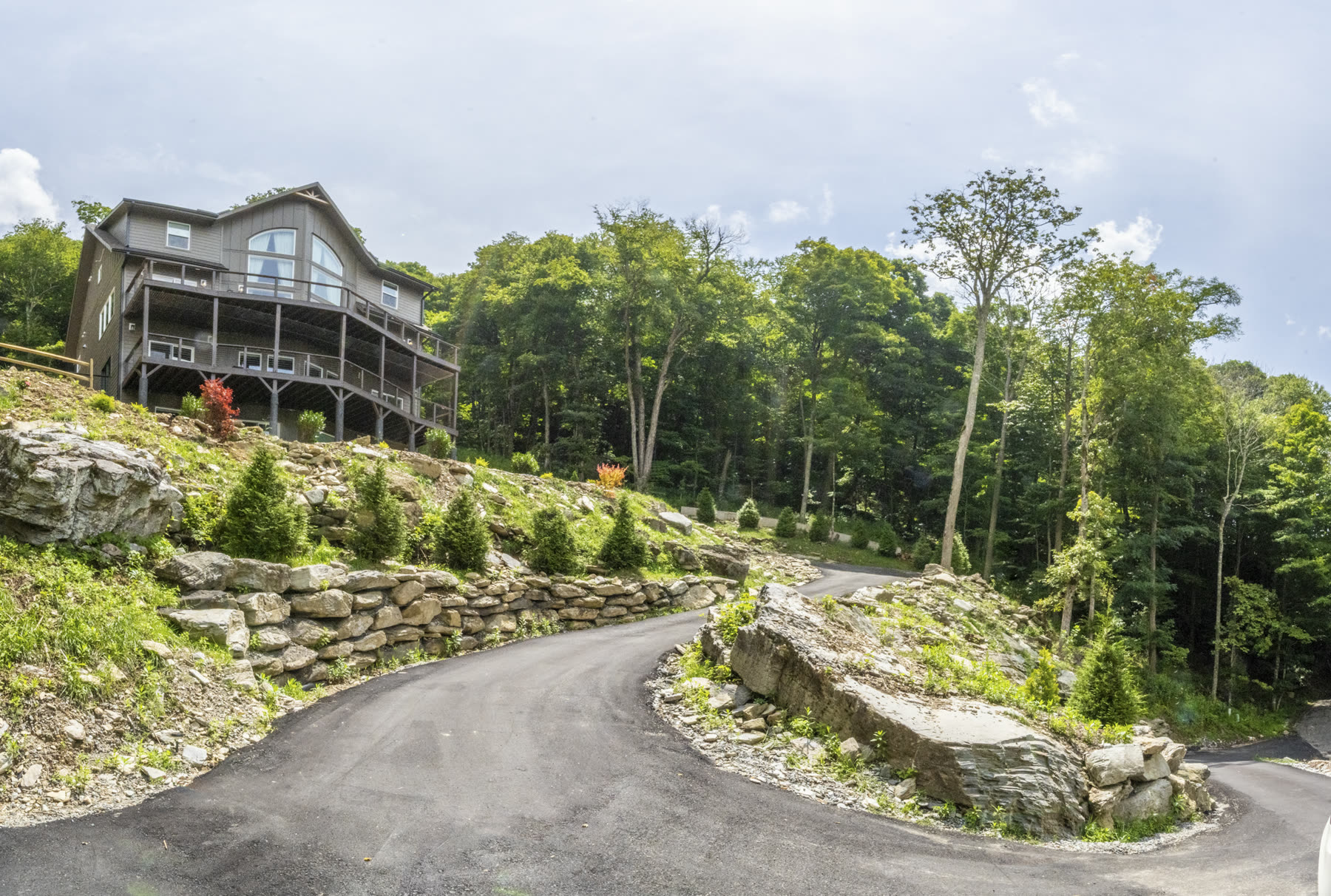 Winding paved driveway lined with natural stone walls leading up to the mountain home