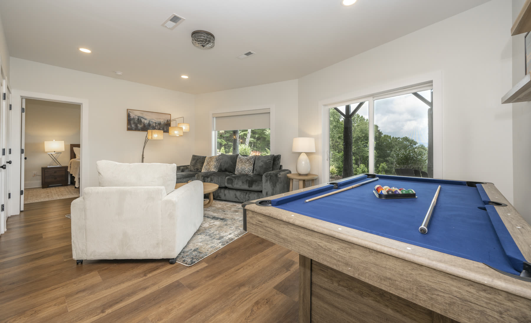 Game room with a blue felt pool table beside large windows looking into the forest