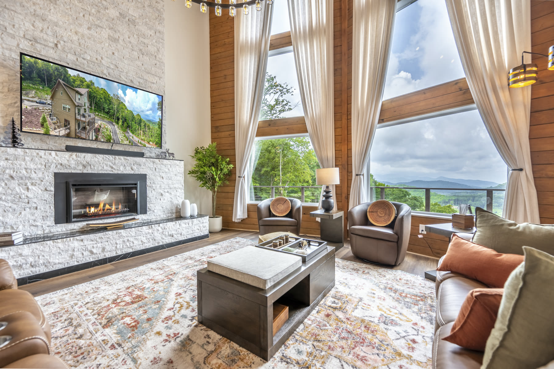 Vaulted great room with stone fireplace, floor-to-ceiling windows, and distant mountain views