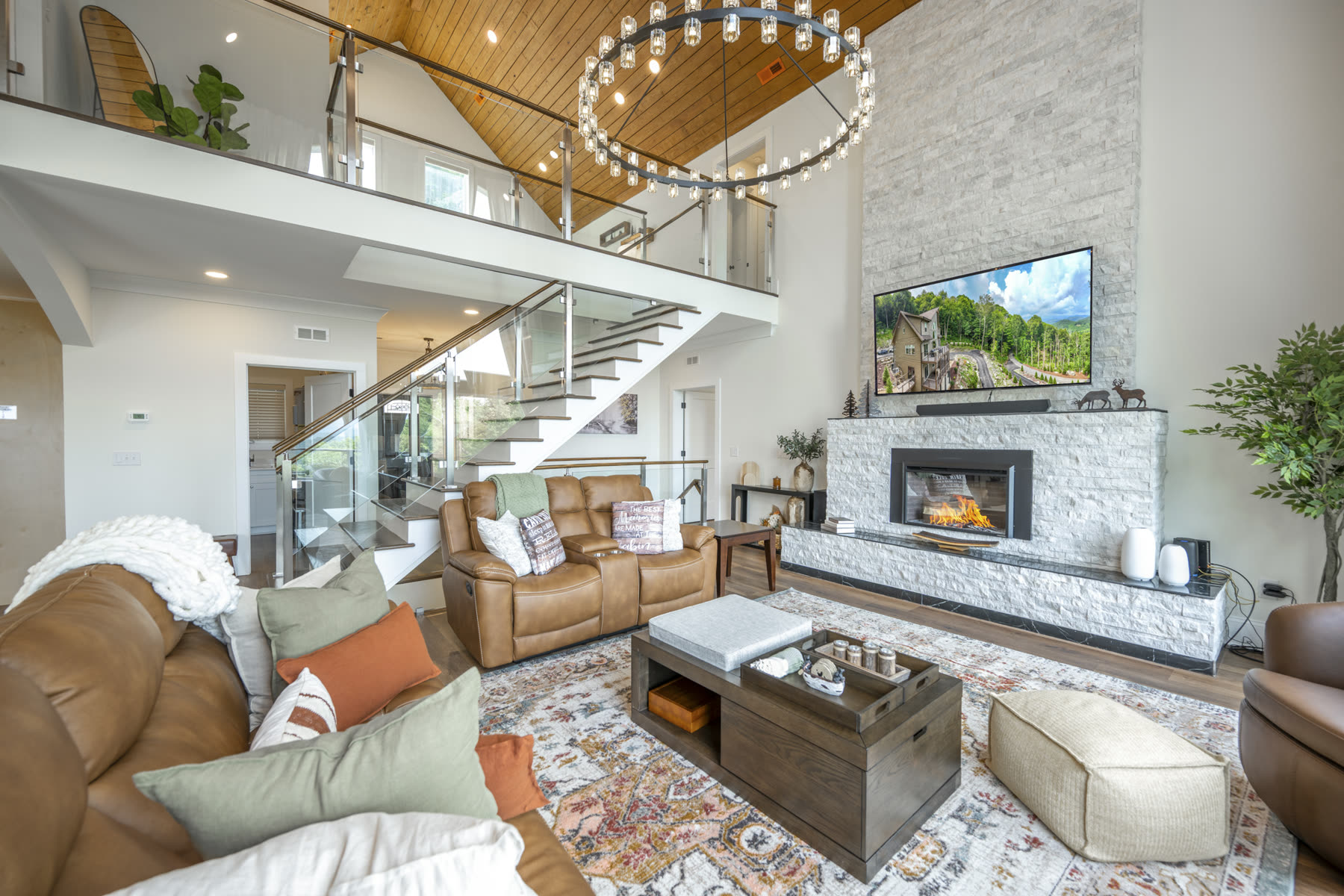 Two-story great room with open staircase, glass railing loft, and a large statement chandelier