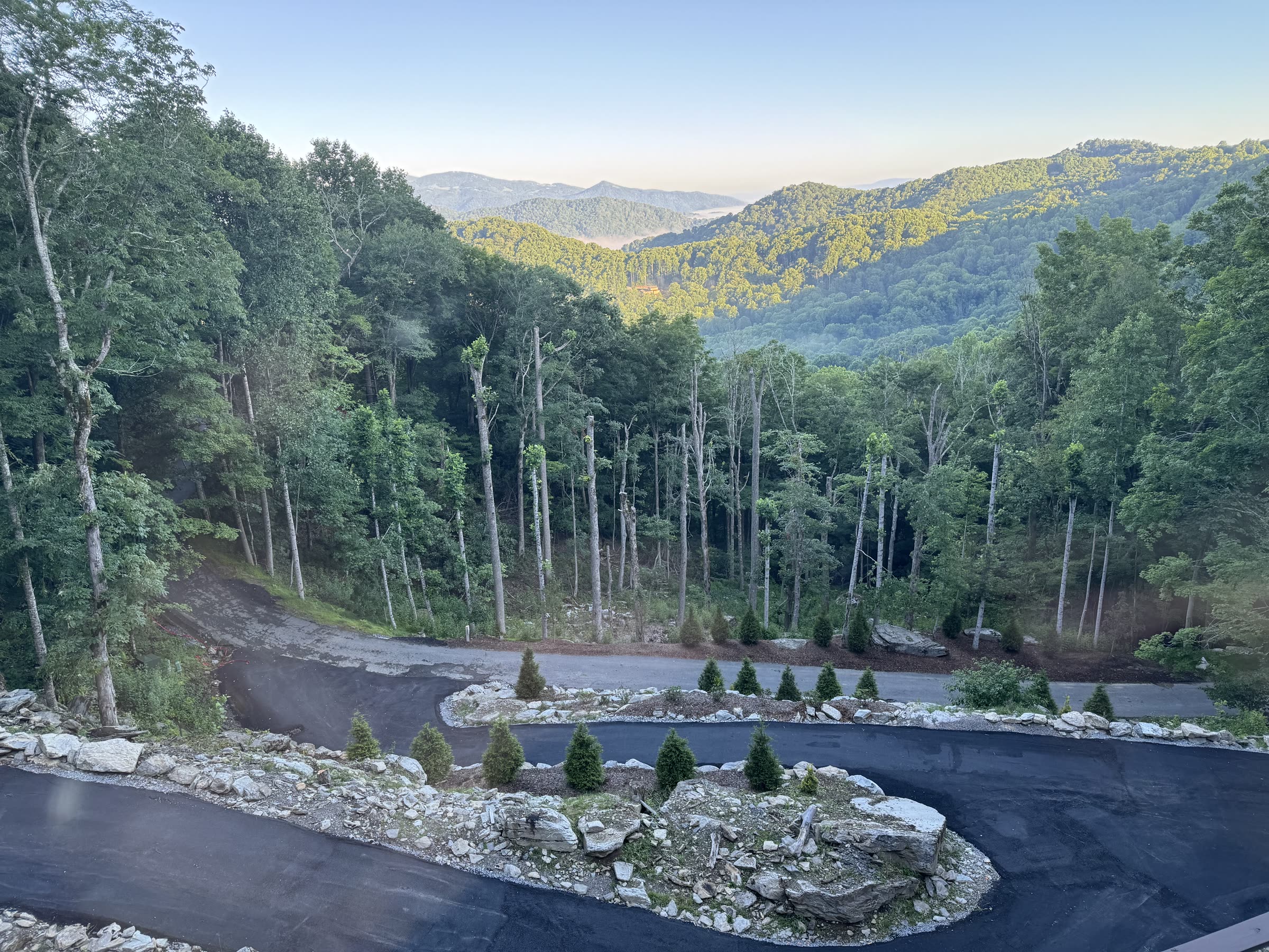 Sunrise over rolling forested mountains with a paved overlook in the foreground