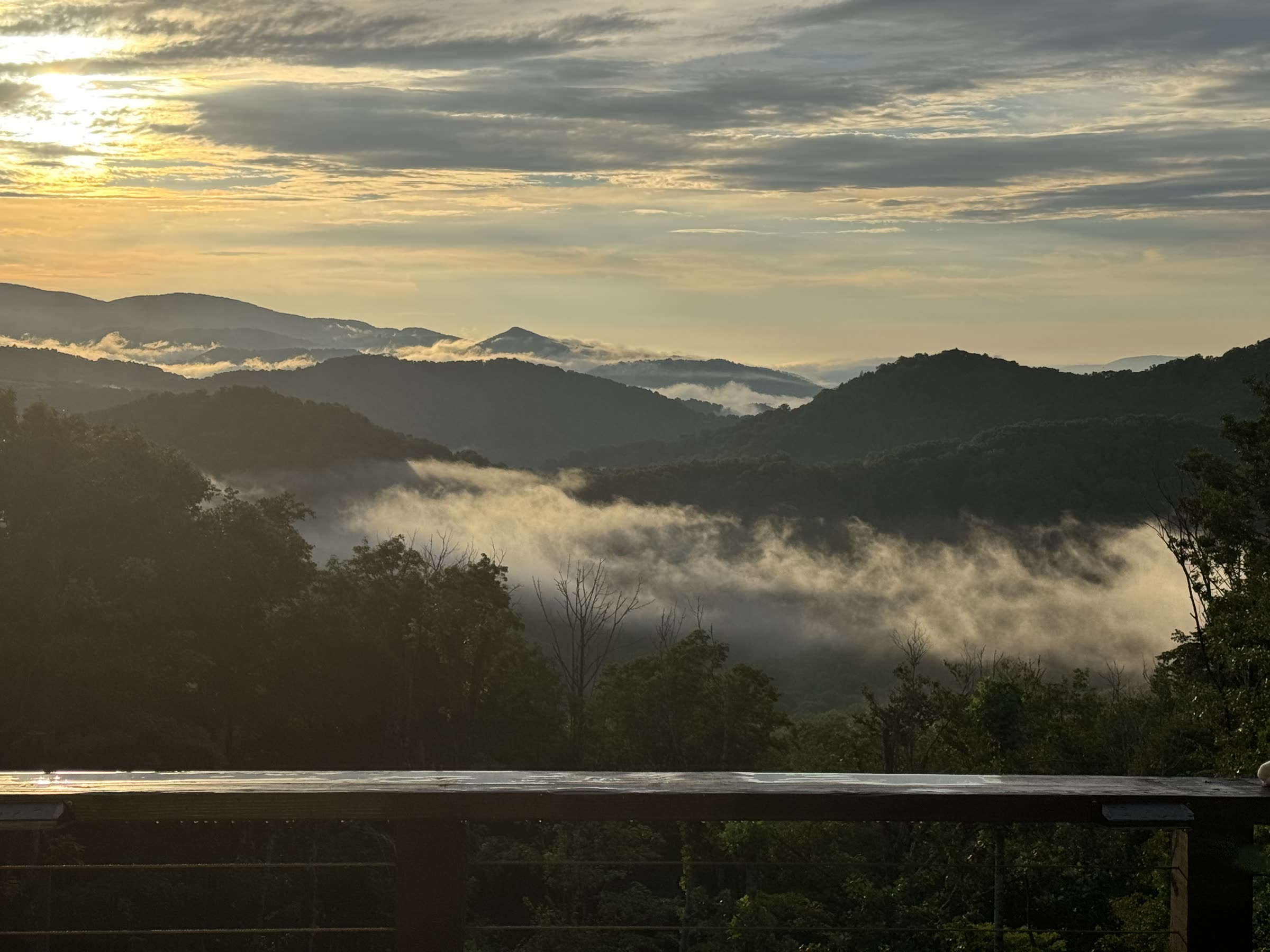 Golden-hour view of fog rolling through the Blue Ridge Mountain valleys, seen from the home's deck railing